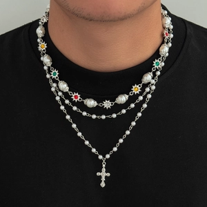 Dettaglio della collana a strati con ciondolo a croce, perle e accenti floreali