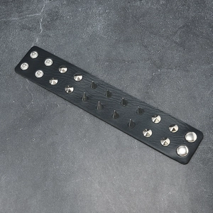 Détail d'un bracelet punk en cuir noir orné de pointes métalliques et de boutons-pression