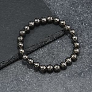 Macro shot of polished dark grey hematite beads on slate surface, 8mm beaded bracelet