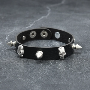 Détail macro du bracelet punk en cuir noir avec têtes de mort argentées et pointes métal