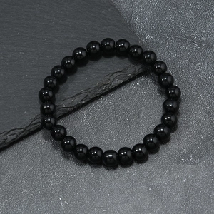 Detail of polished black agate beaded bracelet on a textured dark grey stone surface