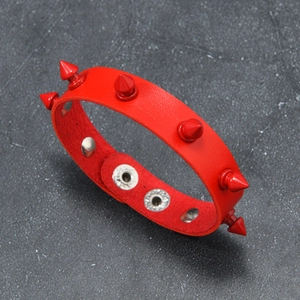 Macro shot of red leather punk bracelet featuring cone spikes and silver snap button closure