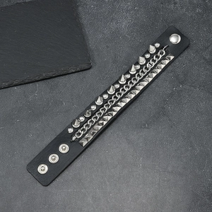 Punk rock black leather bracelet featuring metal studs and chains on a stone background