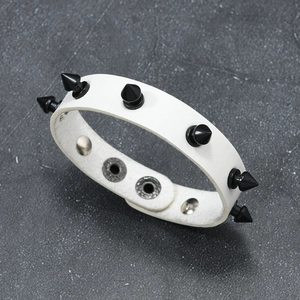 Detail of white leather punk bracelet featuring black conical studs and silver snap buttons