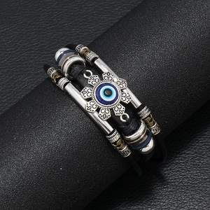 Dettaglio di un bracciale in pelle multistrato con ciondolo malocchio e metallo