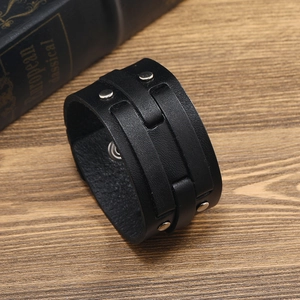 Macro shot of wide black leather punk bracelet with silver metal rivets on a wooden surface