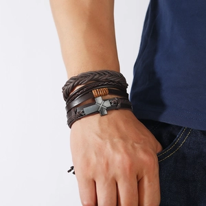 Detail of layered brown leather bracelets with vintage alloy cross charm worn by a male model