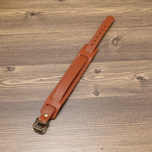 Vintage brown leather wristband with bronze buckle and rivets on wooden surface