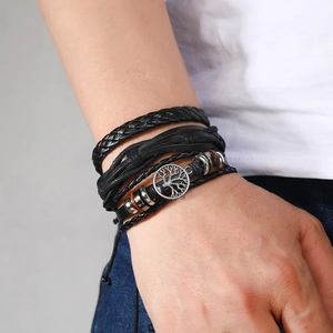 Detail of multi-layer black braided leather bracelet with silver tree of life charm