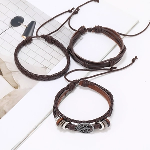 Detail of three-piece brown woven leather bracelet set with tree of life metal charm