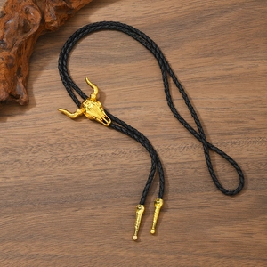 Western bolo tie with gold bull skull pendant and black braided leather cord on wood