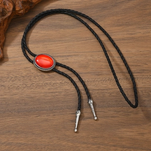 Detail of vintage bolo tie with red stone inlay and engraved silver metal tips on wood