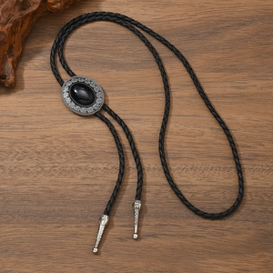 Detail of vintage Celtic bolo tie with black oval stone on a rustic wooden surface