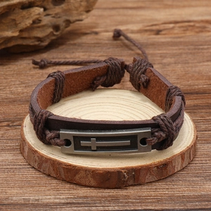Vintage men's brown braided leather bracelet featuring a metal cross charm on wood base
