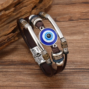 Macro detail of multi-layer leather bracelet with blue evil eye bead on wooden background