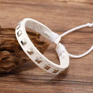 Detailed macro of white leather bracelet with square silver studs on wooden block