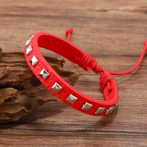 Detail of red leather bracelet with silver pyramid studs and adjustable cord on wood