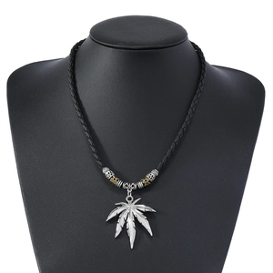 Detailed view of the hemp leaf pendant on a black braided leather necklace