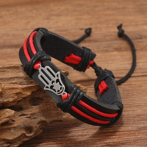 Close-up of leather Hamsa hand bracelet with red woven cords on a rustic wooden base