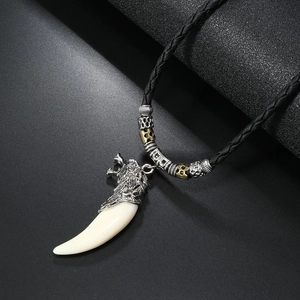 Macro detail of faux ivory fang pendant with engraved wolf head on black braided rope