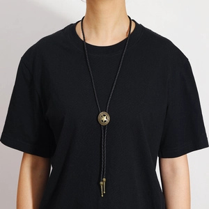 Detail of vintage bronze bolo tie with star pattern on black woven cord worn by model