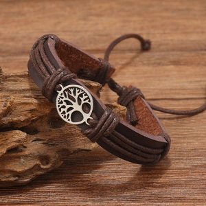 Macro detail of brown braided leather bracelet with Tree of Life charm on wood