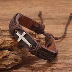 Detail view of a vintage braided brown leather bracelet with silver cross on wood