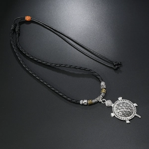 Detailed close-up of alloy turtle pendant with orange bead on woven cord necklace