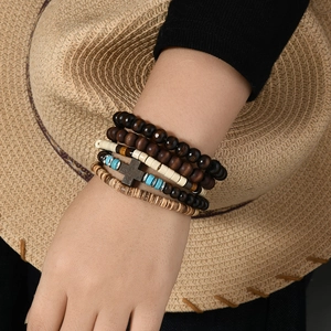 Detail of layered bohemian bracelets featuring wooden beads and a black cross pendant