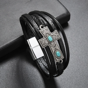 Detail of cross charm with turquoise inlay on multi-layer black leather bracelet