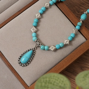 Bohemian turquoise beaded necklace featuring a large teardrop pendant on a velvet tray