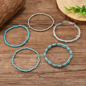 Five-piece bohemian turquoise bead bracelet set and silver cuff on a wooden background