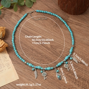 Détail du collier bohème turquoise avec breloques fleurs et plumes argentées sur bois