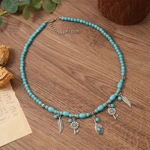 Collier bohème en perles de turquoise avec pendentifs plumes argent sur fond bois