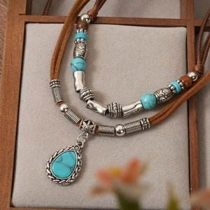 Bohemian multi-layer necklace with turquoise teardrop pendant and braided cord on grey display