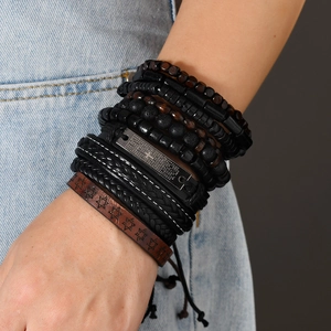 Close-up of stacked leather bracelets with wood beads, cross charm and religious engraving