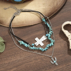 Detail van bohemien gelaagde ketting met turquoise kruis en cactus hangers op hout