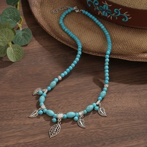 Detail of turquoise beaded necklace with delicate silver leaf pendants on wooden surface