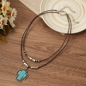 Detail of bohemian turquoise cross pendant with layered brown leather cord on a vintage plate