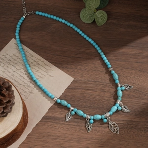 Detail of bohemian turquoise beaded necklace with a silver hollow leaf pendant on wood