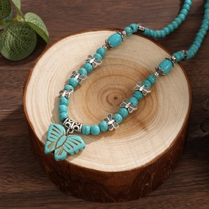 Collier bohème en perles de turquoise avec pendentif papillon argenté sur support en bois