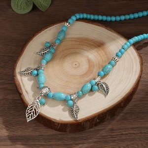 Bohemian turquoise beaded necklace featuring silver hollow leaf pendants on a wood display