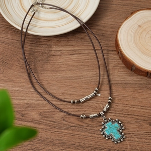Detailed view of turquoise cross pendant on vintage double-layer leather cord necklace