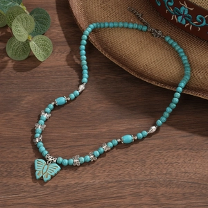 Détail macro du collier en perles de turquoise avec pendentif papillon et décor de bois