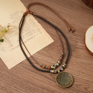 Détail macro d'un pendentif totem en bronze sur collier en cuir tressé avec perles en bois