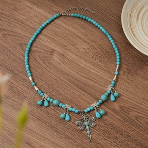 Detail of bohemian turquoise beaded necklace featuring a large dragonfly pendant on wood