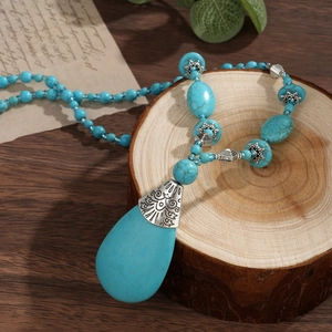 Detail of bohemian turquoise necklace with large teardrop pendant on vintage wood background