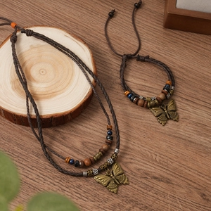Detail of bohemian multilayer braided necklace with bronze butterfly pendant on wood