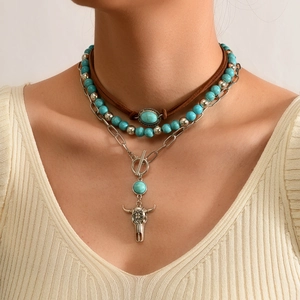 Detail van gelaagde turquoise kralenkettingen met een vintage zilveren stierenkop