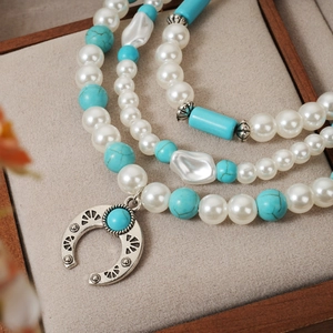 Macro detail of multi-layer turquoise pearl necklace with vintage horseshoe pendant